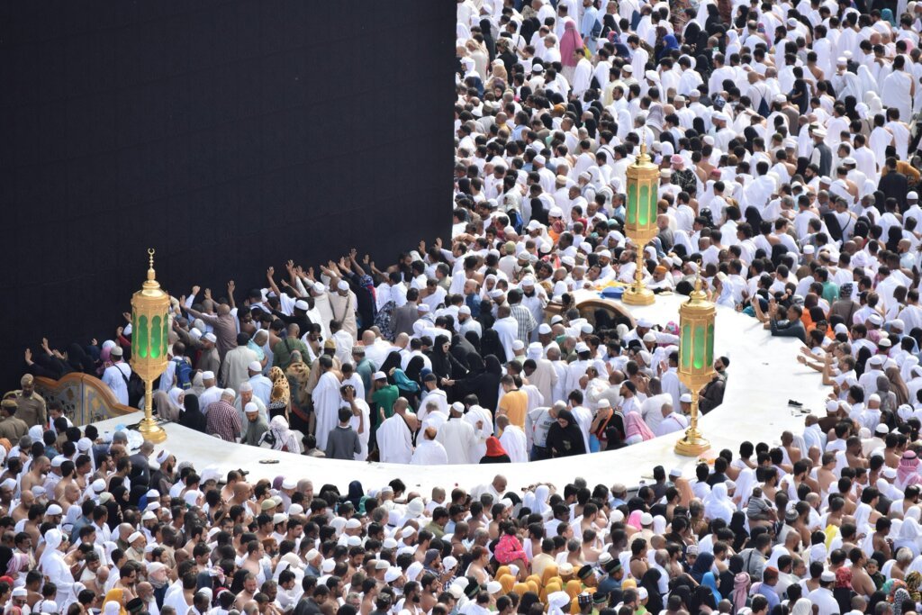 Men and women dressed in white Ihram garments preparing for Hajj rituals at Masjid al-Haram.